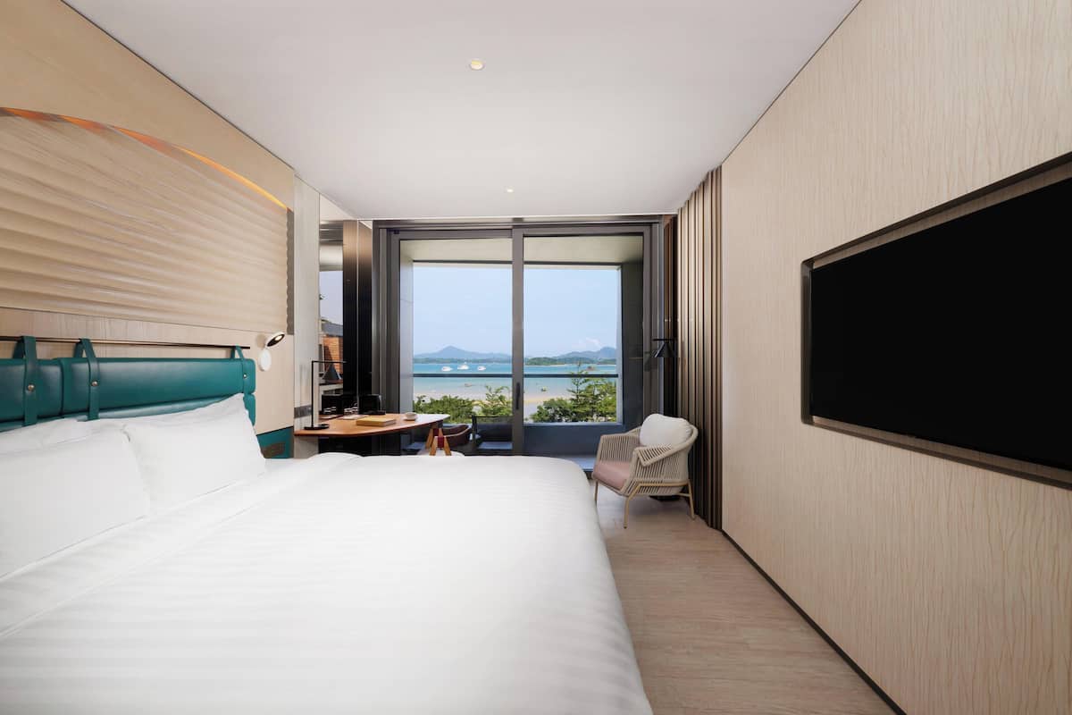 Ein modernes Hotelzimmer mit einem großen Bett, einem Schreibtisch, einem Stuhl und einem Fernseher.