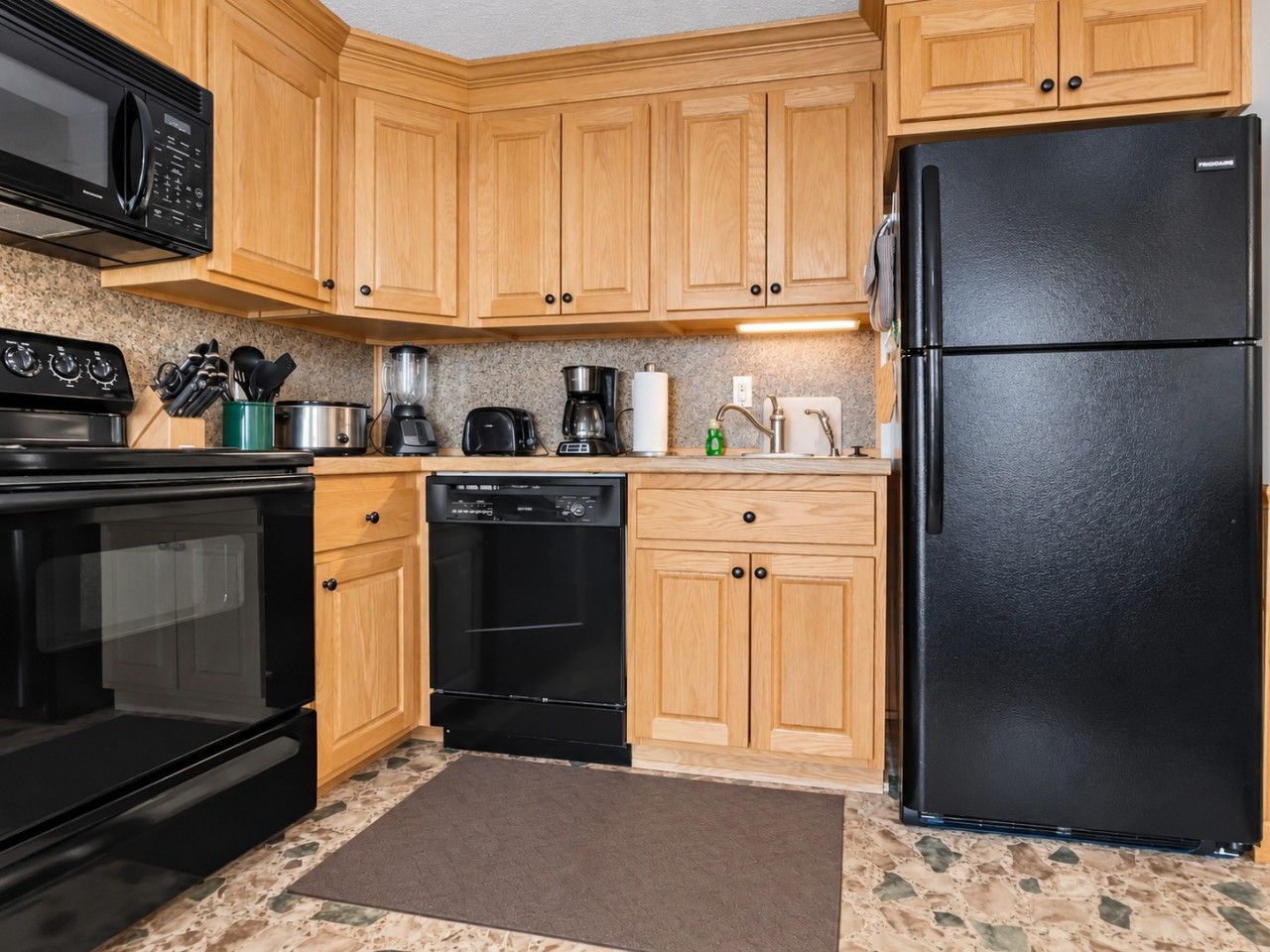 Una cocina con armarios de madera, un refrigerador negro, una estufa negra y un lavavajillas.