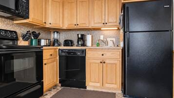 Una cocina con armarios de madera, un refrigerador negro, una estufa negra y un lavavajillas.