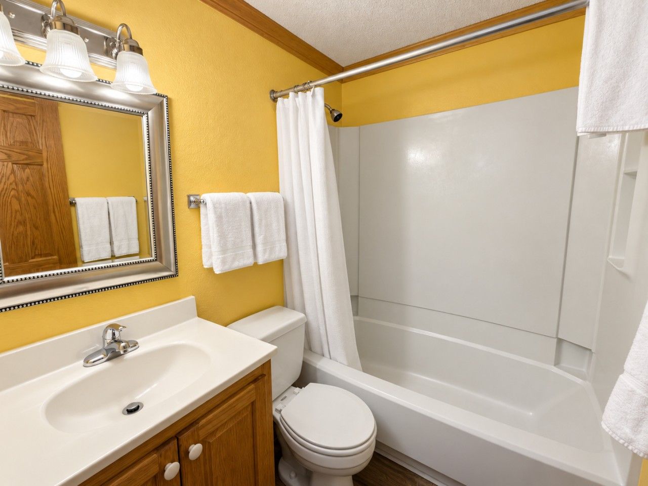 A bathroom with a white sink, mirror, and toilet, a shower with a curtain, and towels hanging on the wall.