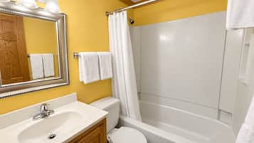 A bathroom with a white sink, mirror, and toilet, a shower with a curtain, and towels hanging on the wall.