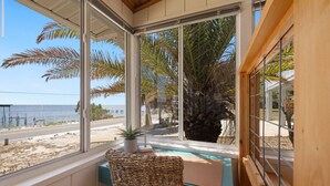 Une chambre avec vue sur la plage et les palmiers, une chaise en osier et un petit bureau avec une lampe.
