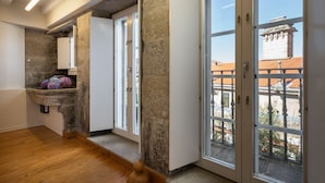 A hallway with stone walls, wooden flooring, and large windows with a view of buildings and a balcony.