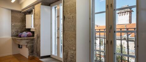 Un pasillo con paredes de piedra, suelo de madera y grandes ventanas que ofrecen vistas a edificios y un balcón.