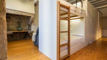 A bunk bed room with a stone fireplace, wooden flooring, and a small table with a vase.