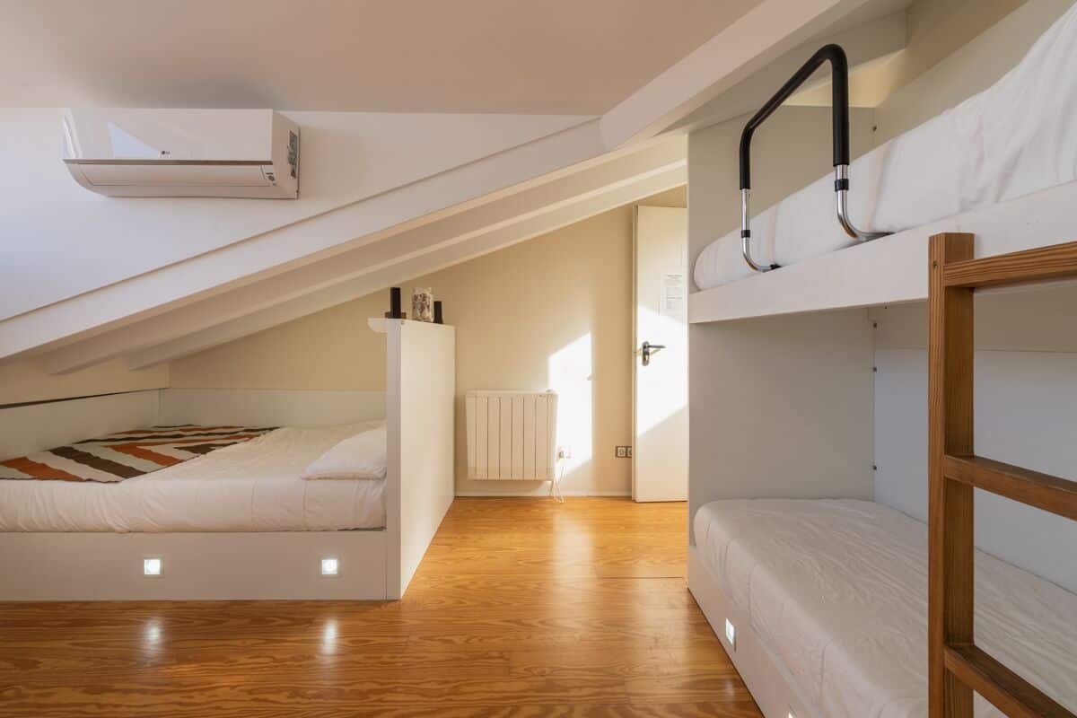 Una habitación moderna y compacta con literas, un radiador blanco y un equipo de aire acondicionado.
