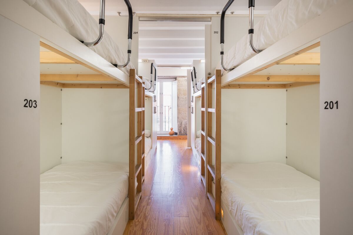 A corridor with bunk beds numbered 203 and 201, wooden flooring, and a view into a room with a window.