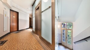 A hotel corridor with a patterned carpet, wooden doors, and a glass door leading to a balcony with a view of greenery. - Stylish Apartment in Prague 1 Close to Old Town Square by EasyBNB Premium (Prague)