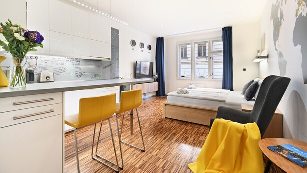 A modern hotel room with a kitchenette, a bed, a desk, and a window with curtains. - Stylish Apartment in Prague 1 Close to Old Town Square by EasyBNB Premium (Prague)