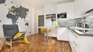 A modern kitchen with white cabinets, a wooden floor, a map wall, and a bar area with a yellow chair. - Stylish Apartment in Prague 1 Close to Old Town Square by EasyBNB Premium (Prague)