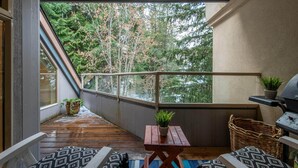 A balcony with a wooden floor, a small table with a plant, a wicker basket, and a grill. - 31GlenEagle Cozy Townhome | 2 Bedroom 2 Bathroom, GlenEagle Townhome Whistler, Golf/Ski community (Whistler)