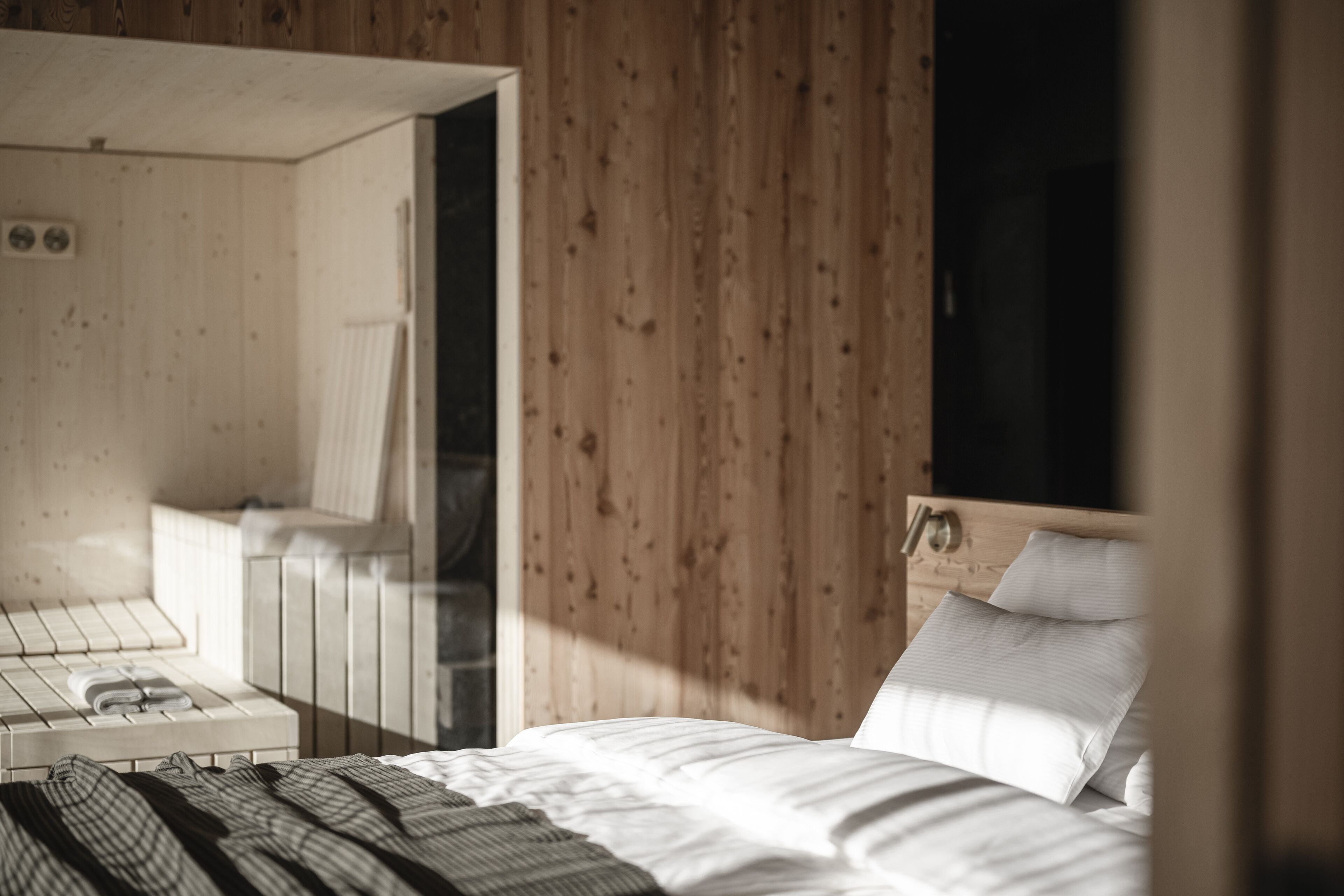 Interior de una cabaña de madera con una cama, un pequeño rincón de descanso y una ventana.
