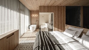 A modern bedroom with a large bed, a built-in bench, a bathtub, and a wooden ceiling. - OLM Nature Escape - Eco Aparthotel (Campo Tures)