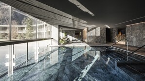 A modern indoor pool area with a glass wall, marble flooring, and a staircase leading to a higher level. - OLM Nature Escape - Eco Aparthotel (Campo Tures)