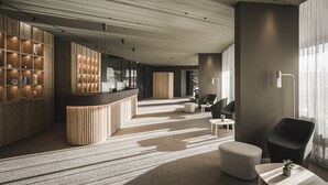 A modern hotel lobby with a reception desk, wooden shelving, seating area, and a staircase. - OLM Nature Escape - Eco Aparthotel (Campo Tures)