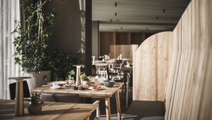 A dining area with wooden tables and chairs, a potted plant, and a view of the adjacent room. - OLM Nature Escape - Eco Aparthotel (Campo Tures)