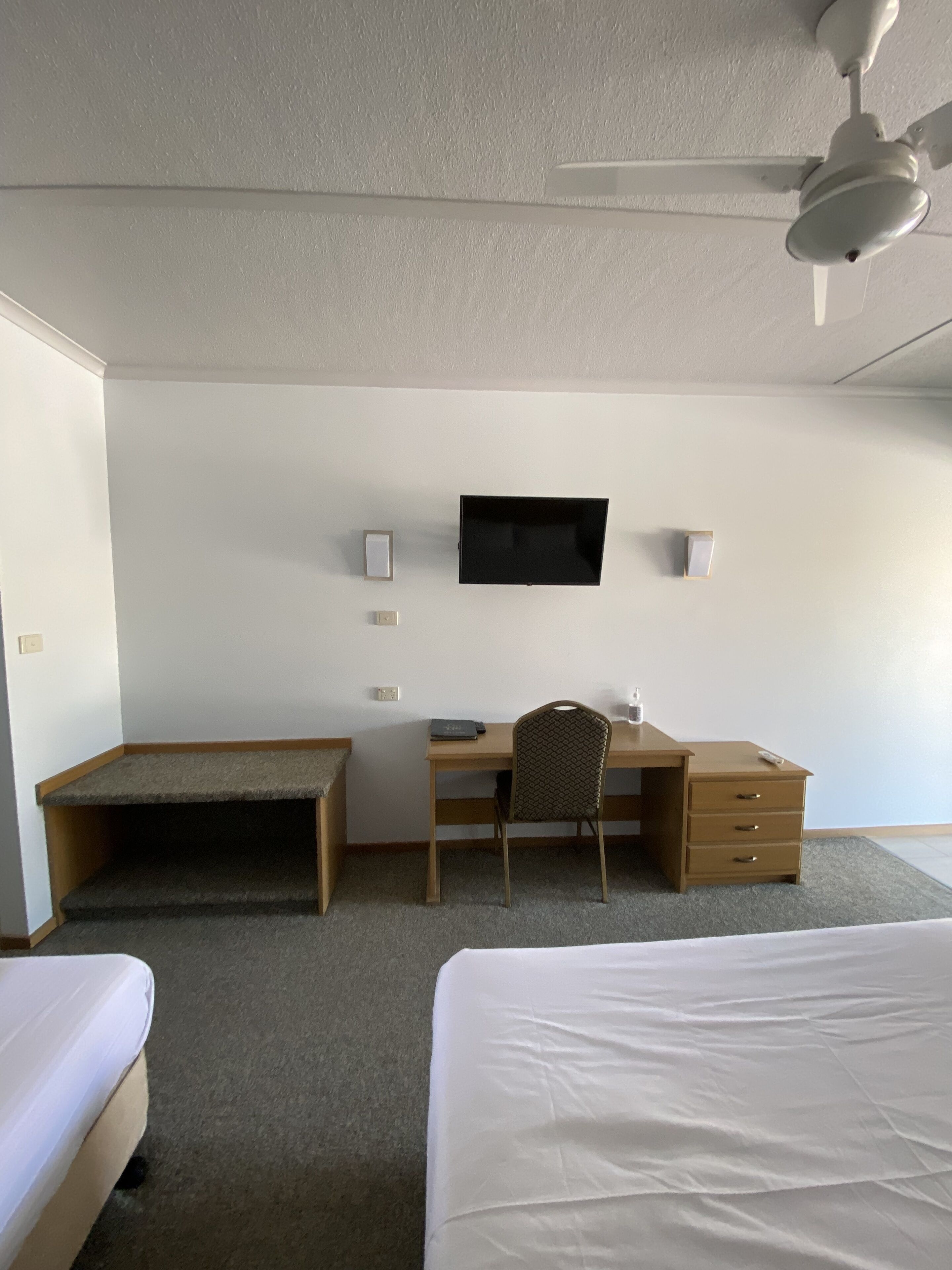 A hotel room with a bed, a desk, a chair, a television, and a ceiling fan.
