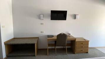 A hotel room with a bed, a desk, a chair, a television, and a ceiling fan.