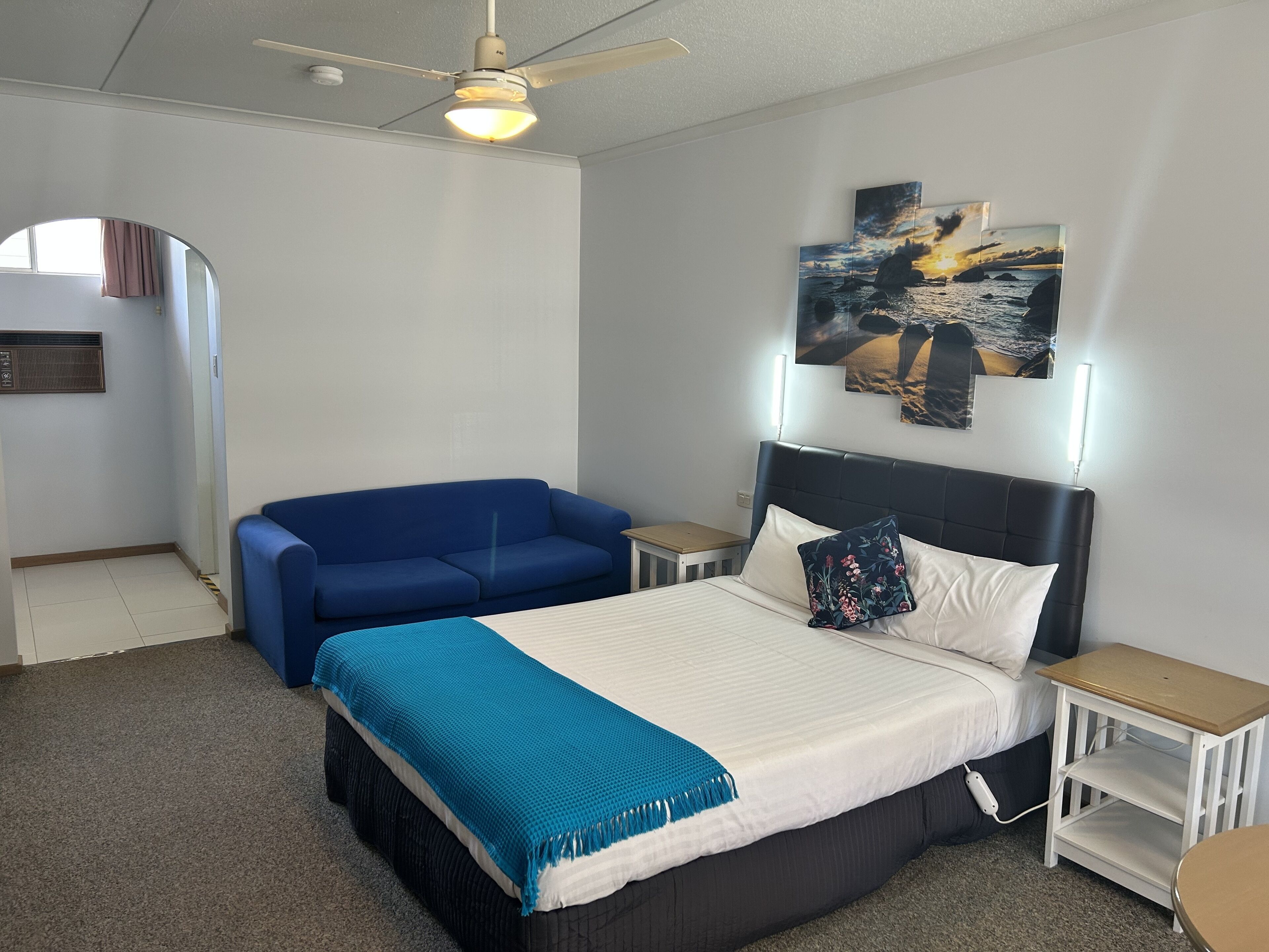 Quarto com cama, sofá azul, ventoinha no teto e obras de arte nas paredes.