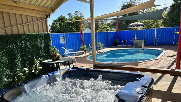 A hot tub with water, a pool, and a covered patio area with chairs and tables.