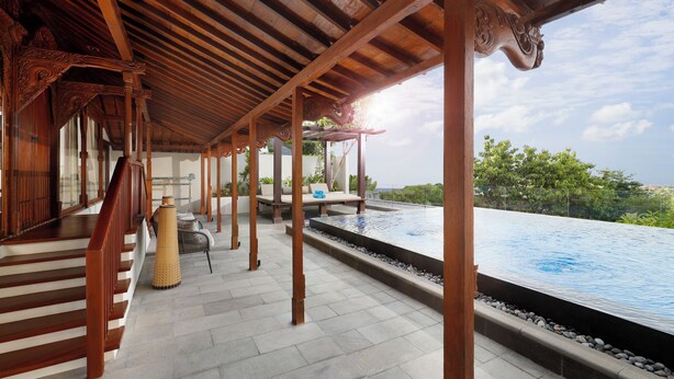 Uma área externa coberta com piscina, colunas de madeira e uma escadaria.