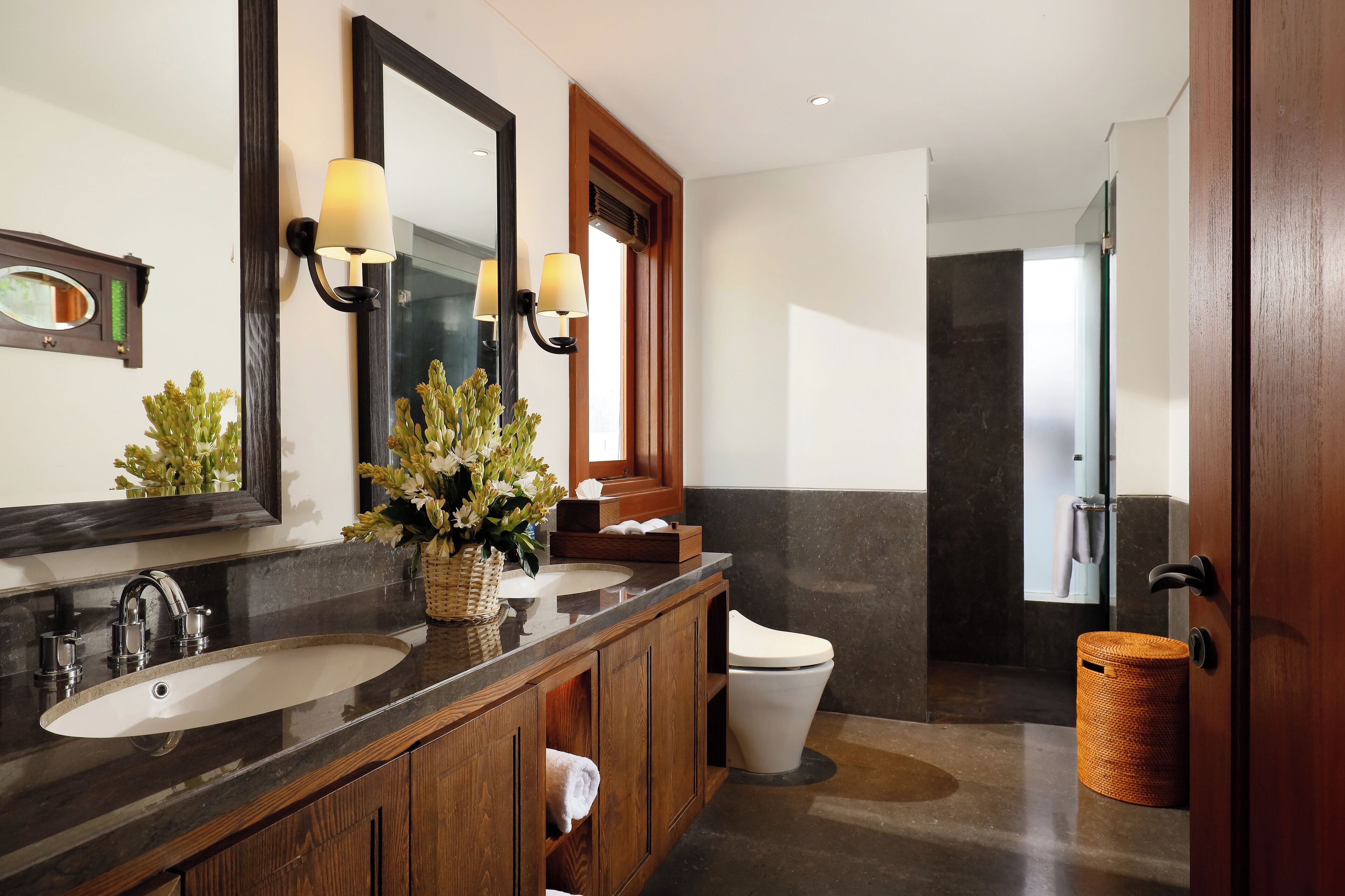 A modern bathroom with a dark marble countertop, two sinks, a large mirror, and a toilet.