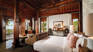 Um quarto espaçoso com uma cama grande, um espaço de estar com sofá e poltronas, teto de madeira e vista para o exterior.