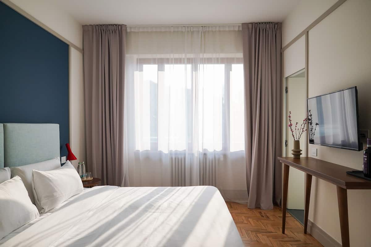 Una habitación de hotel con cama, escritorio, televisor y ventana con cortinas.