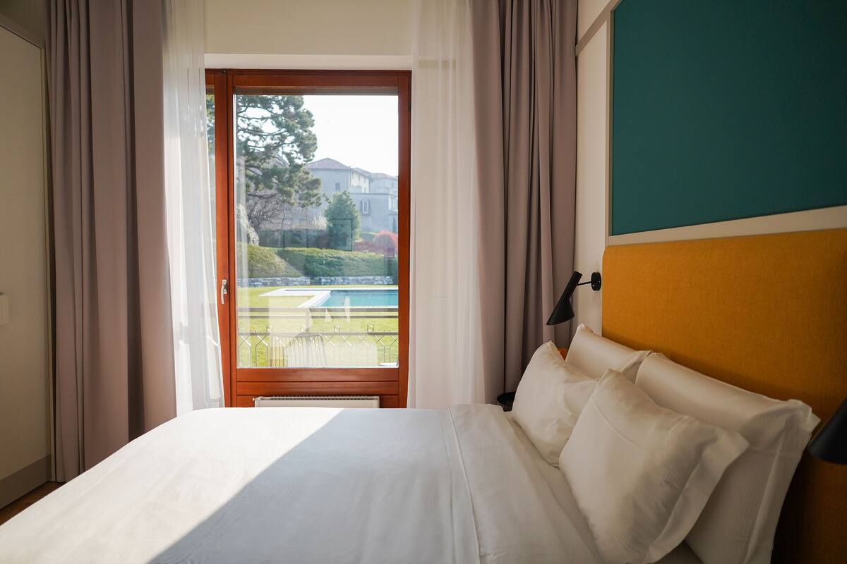 Habitación de hotel con cama, vista a una piscina y balcón.