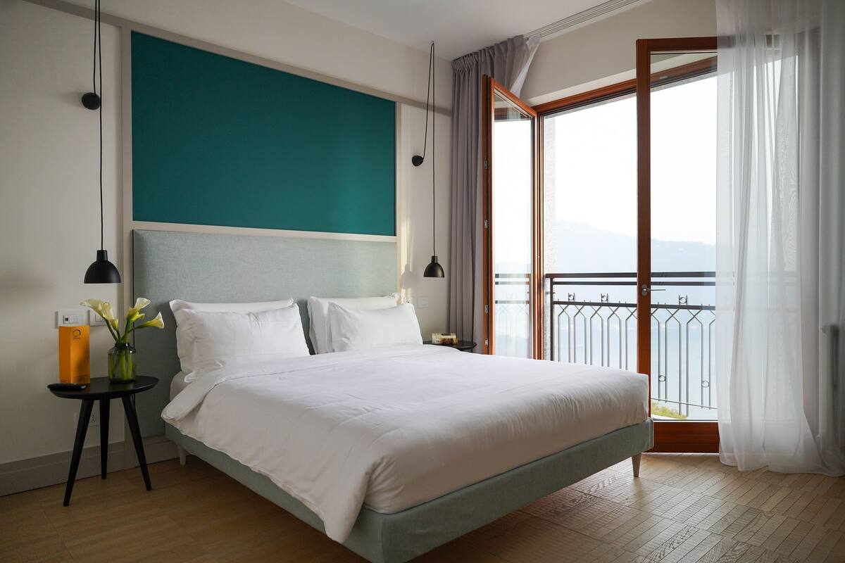 Una habitación de hotel moderna con una cama grande, vista al mar desde un balcón y una pared de acento color aguamarina.