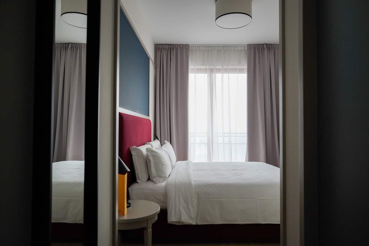 Una habitación de hotel con cama, una mesita redonda y un ventanal con cortinas.