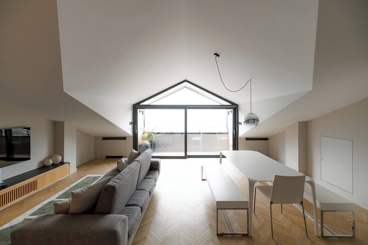 Un loft moderno con techo alto, un tragaluz grande, un sofá, una mesa de comedor y un televisor.