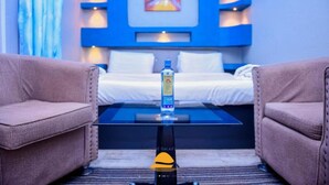 A modern hotel room with a glass coffee table, a bed with white linens, and a blue accent wall.