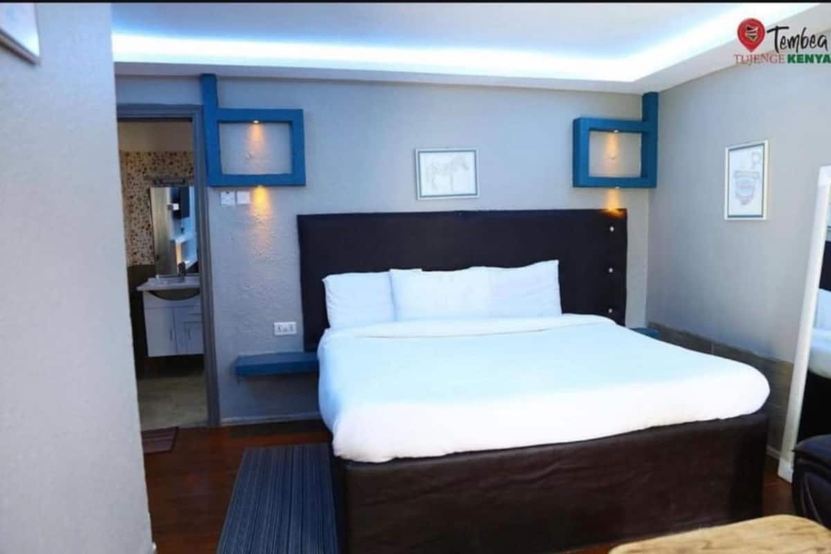 Ett hotellrum med en stor säng, ett litet skrivbord och ett badrum som syns genom en öppen dörr.