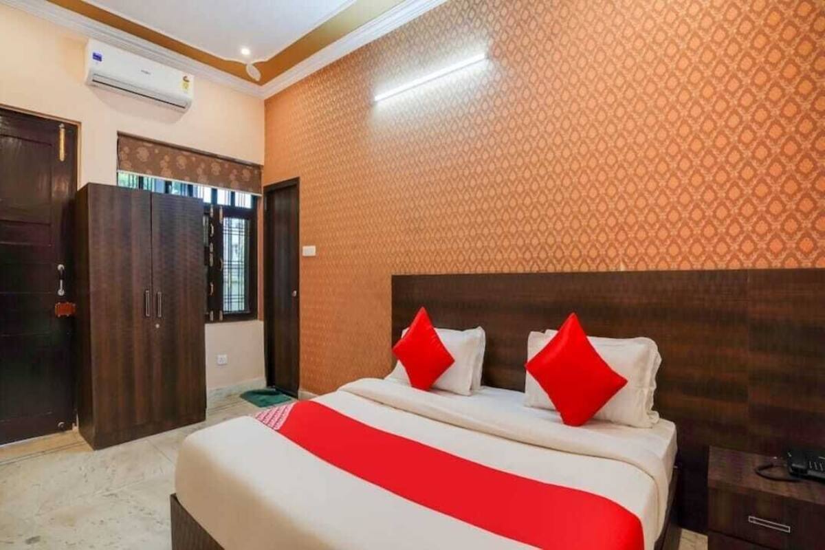 A hotel room with a large bed, two red pillows, a wooden headboard, an air conditioning unit, and a wardrobe.
