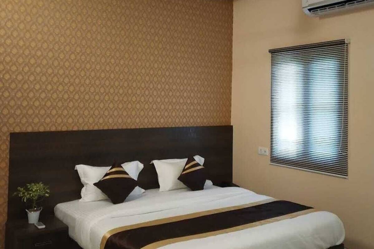 A hotel room with a large bed, a ceiling fan, an air conditioning unit, and a window with blinds.