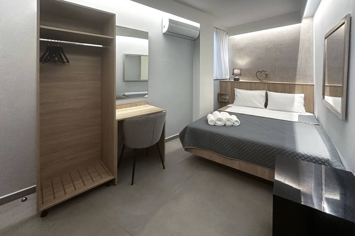A modern hotel room with a bed, a desk, a chair, and a wardrobe.