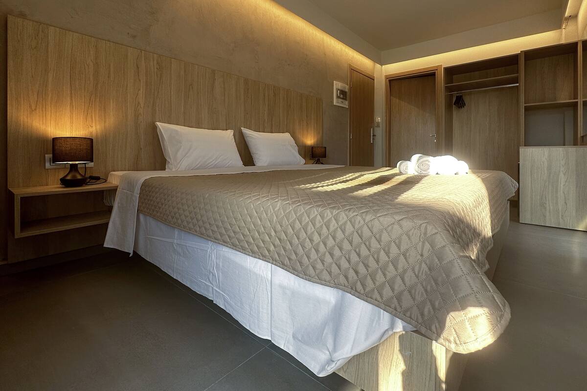 A modern bedroom with a large bed, bedside lamps, a wooden headboard, and built-in wardrobes.