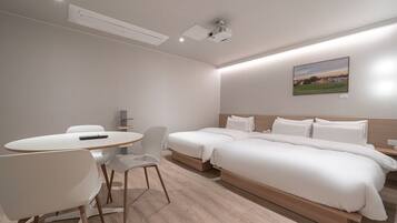 A modern hotel room with a single bed, a small table with chairs, a projector, and a painting on the wall.