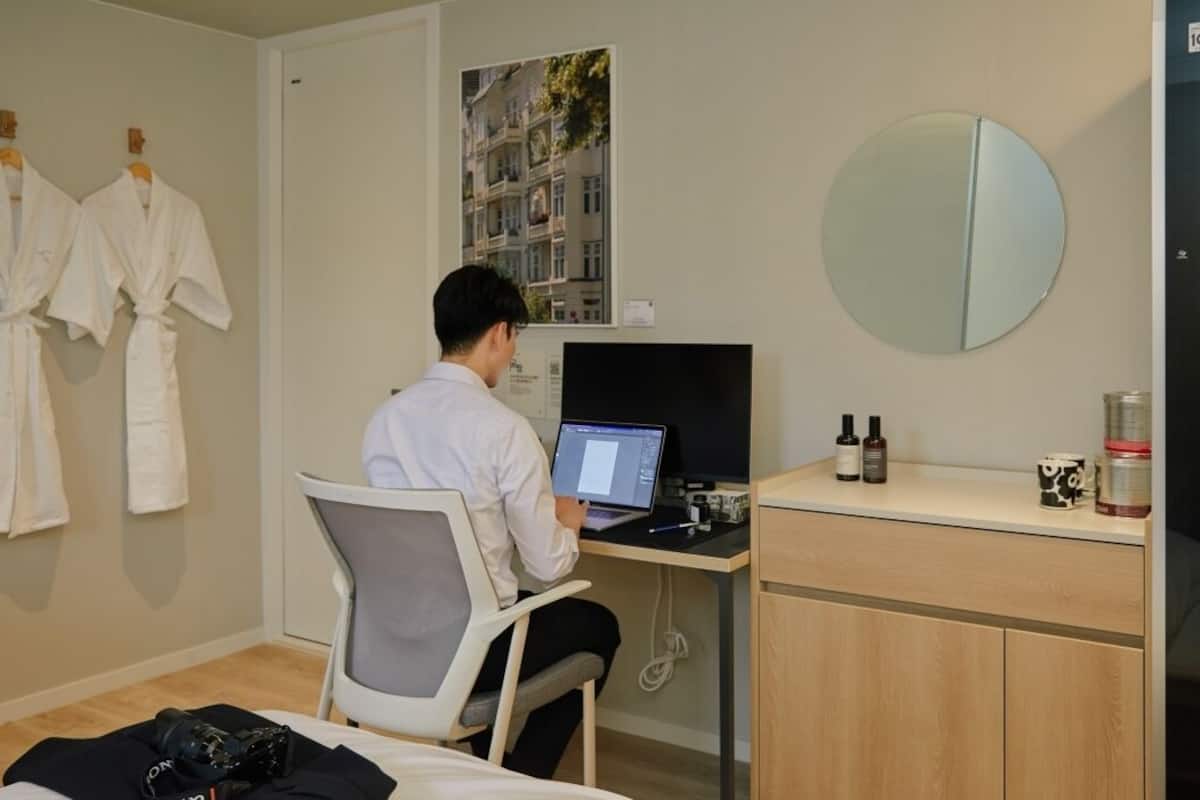 A hotel room with a desk, a laptop, a mirror, and a bed.