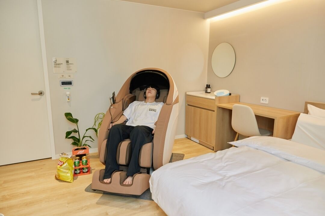 Ein Zimmer mit Massagesessel, Bett, Schreibtisch und Spiegel.
