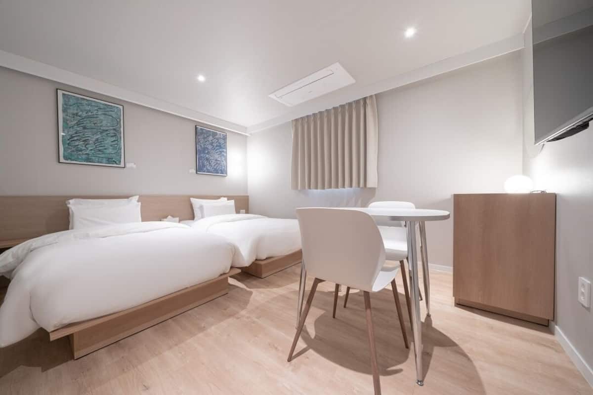 A modern hotel room with a double bed, a desk with a chair, a wardrobe, and two wall-mounted artworks.