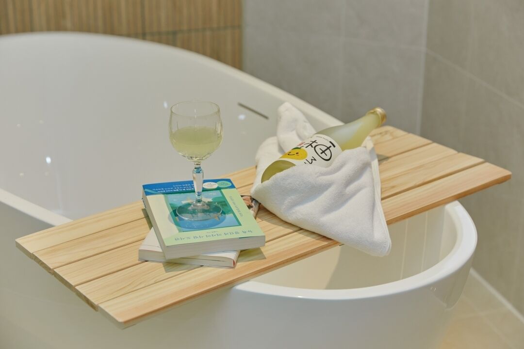 A bathtub with a book and a glass of wine on a wooden tray.