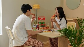 A dining area with two people eating pizza, a table with pizza boxes, a bottle, and a red shelf with drinks. - Anook Thepeak Hotel Incheon Songdo (Incheon)