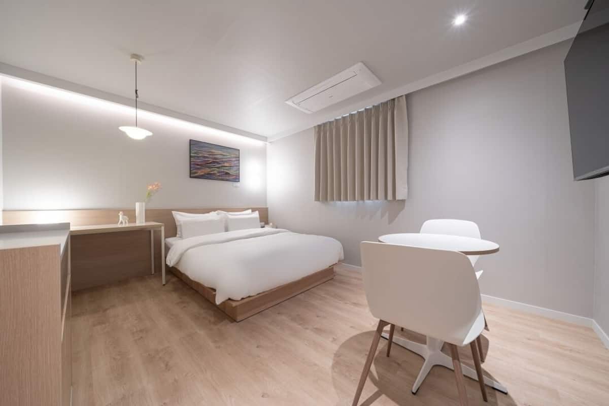A modern hotel room with a bed, bedside table, chair, and a small desk.