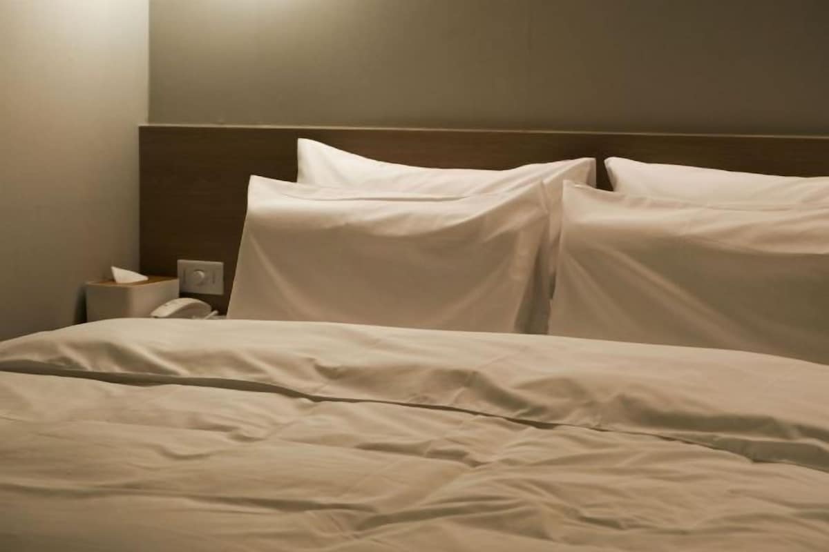 A hotel room with a neatly made bed, a bedside table with a lamp, and a wall-mounted telephone.