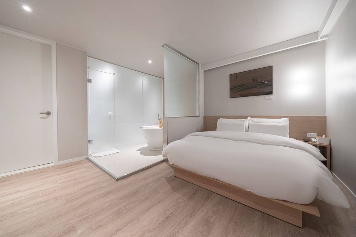 A modern bedroom with a large bed, a walk-in closet, and a glass shower enclosure.