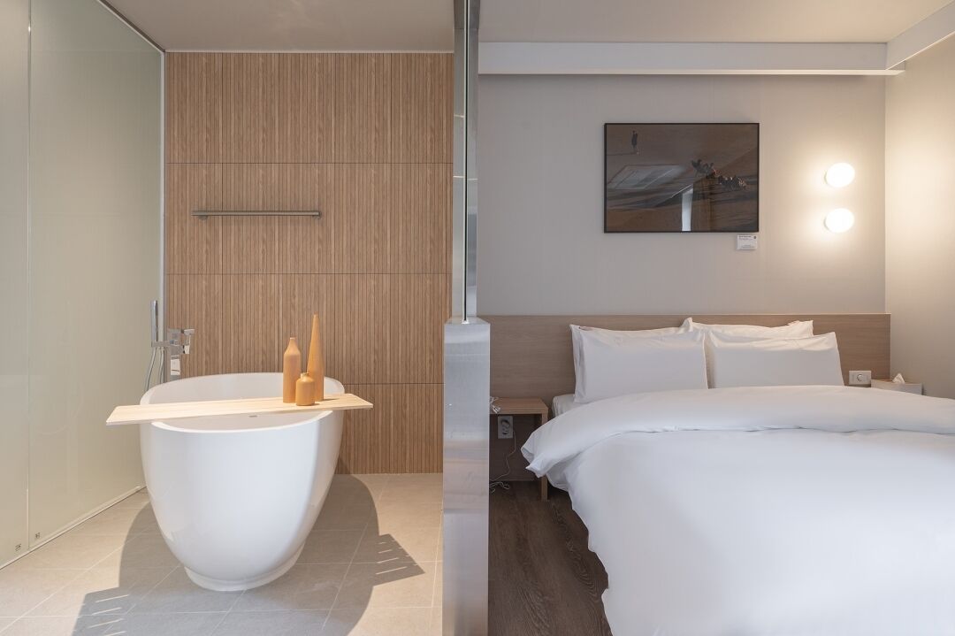 A modern hotel room with a large bathtub, a bed with white linens, and a painting on the wall.