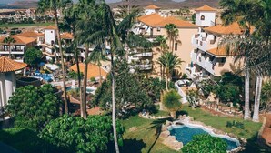 Un resort con varias edificaciones, una piscina y palmeras.