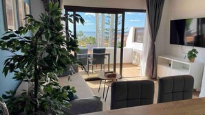 Una sala de estar moderna con una planta grande, una mesa de comedor y vistas al océano a través de un ventanal corredera.